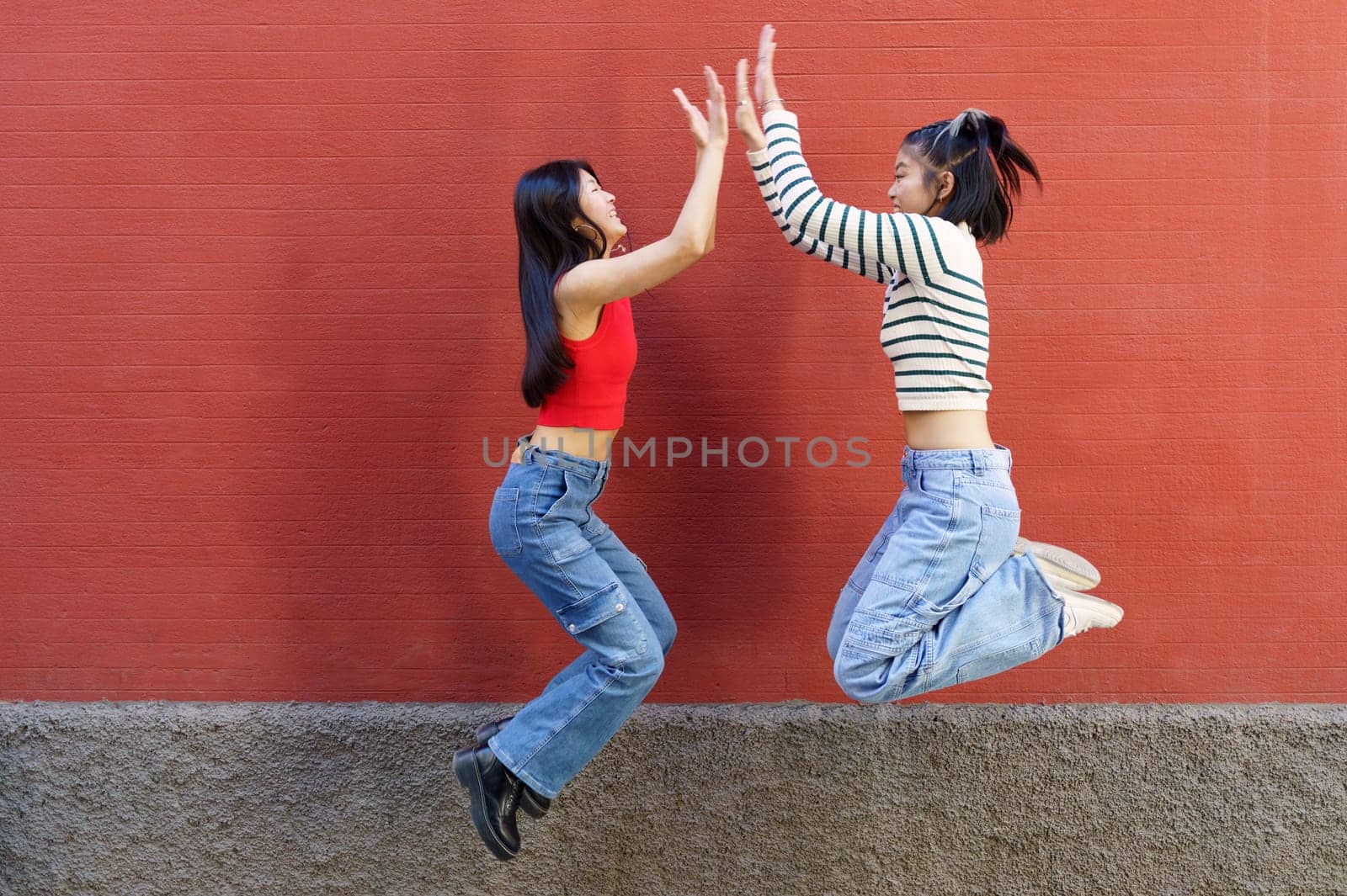 Joyful young Asian girlfriends giving high five while jumping by javiindy