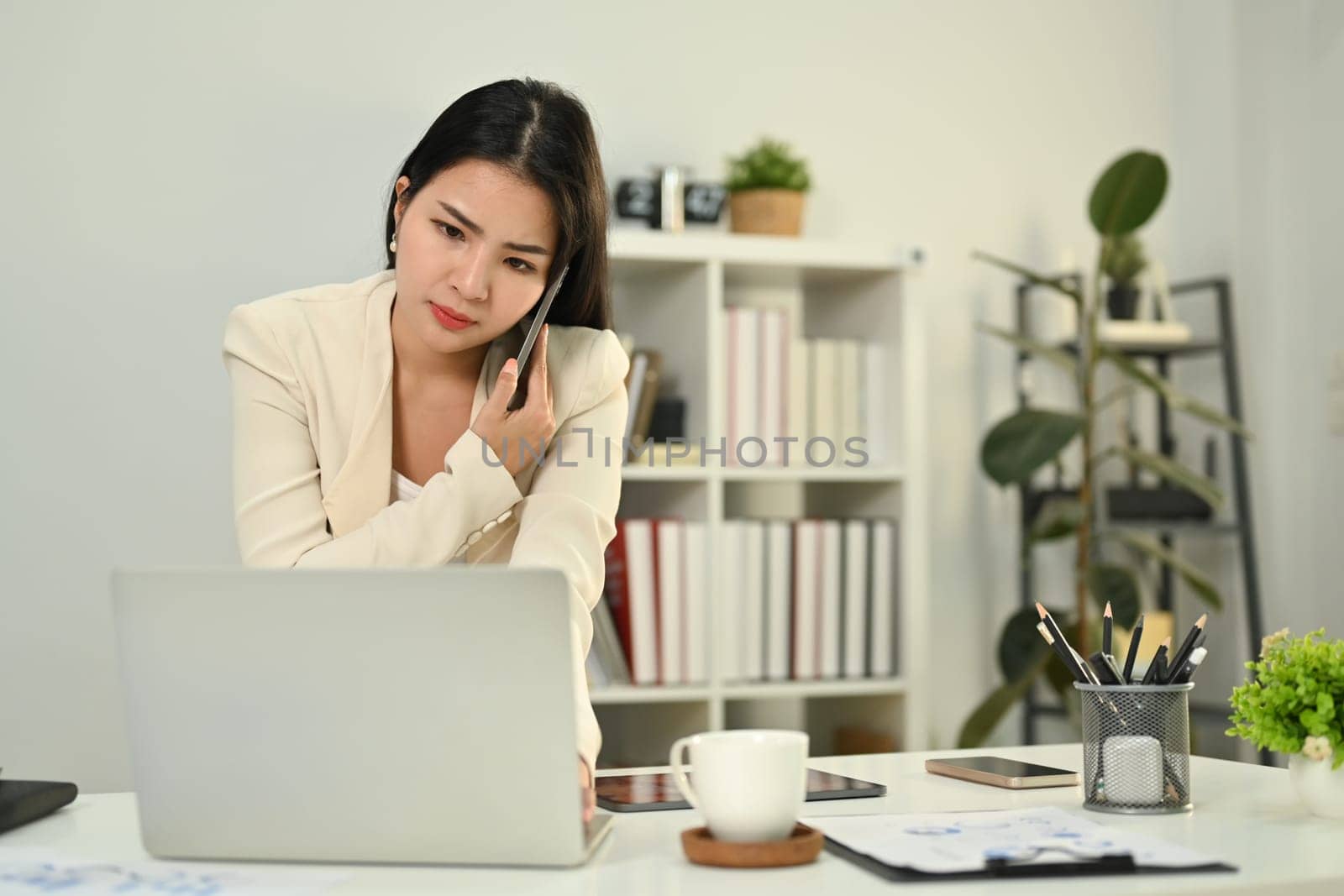 Serious female investment advisor having unpleasant phone conversation, consulting client at working desk.