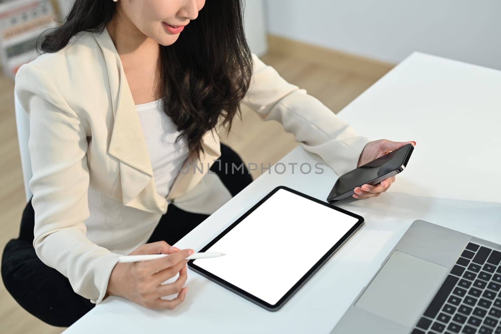 Cropped shot view of young businesswoman hand holding mobile phone and using digital tablet at office desk.