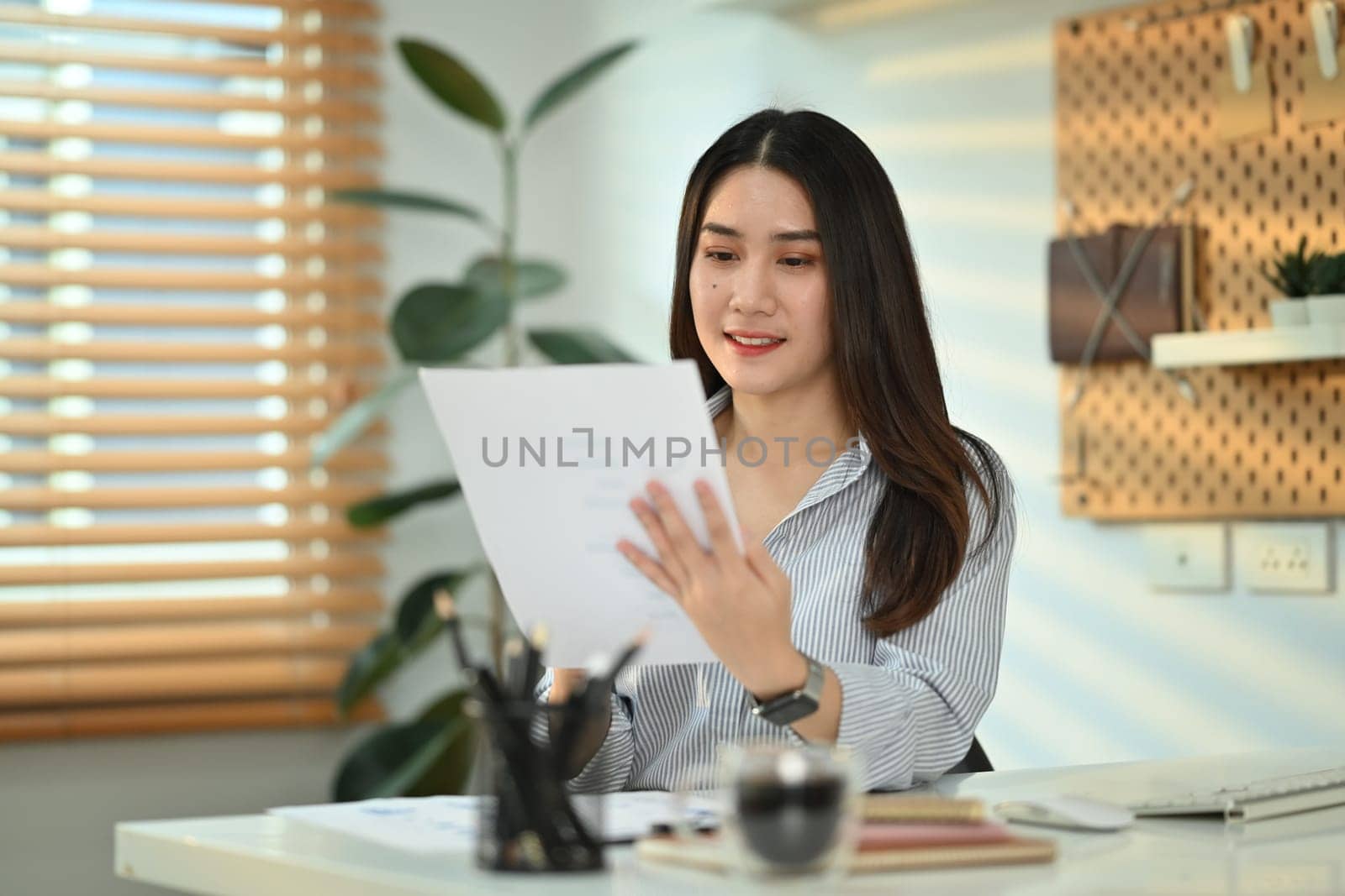 Charming asian female accountant working bookkeeping documents, checking financial data at office by prathanchorruangsak