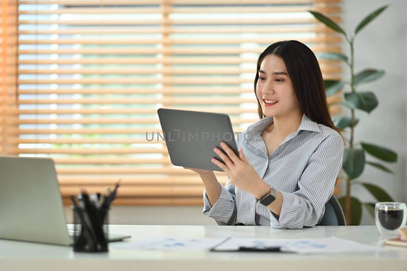 Smiling millennial woman reading email or checking daily routine on digital tablet, sitting in modern home office.