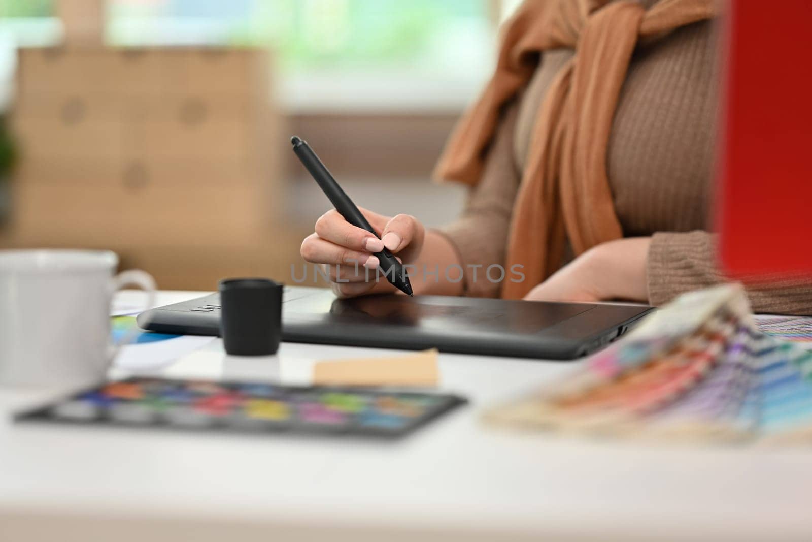Young creative woman using graphic tablet and working with color swatch samples at modern workplace.