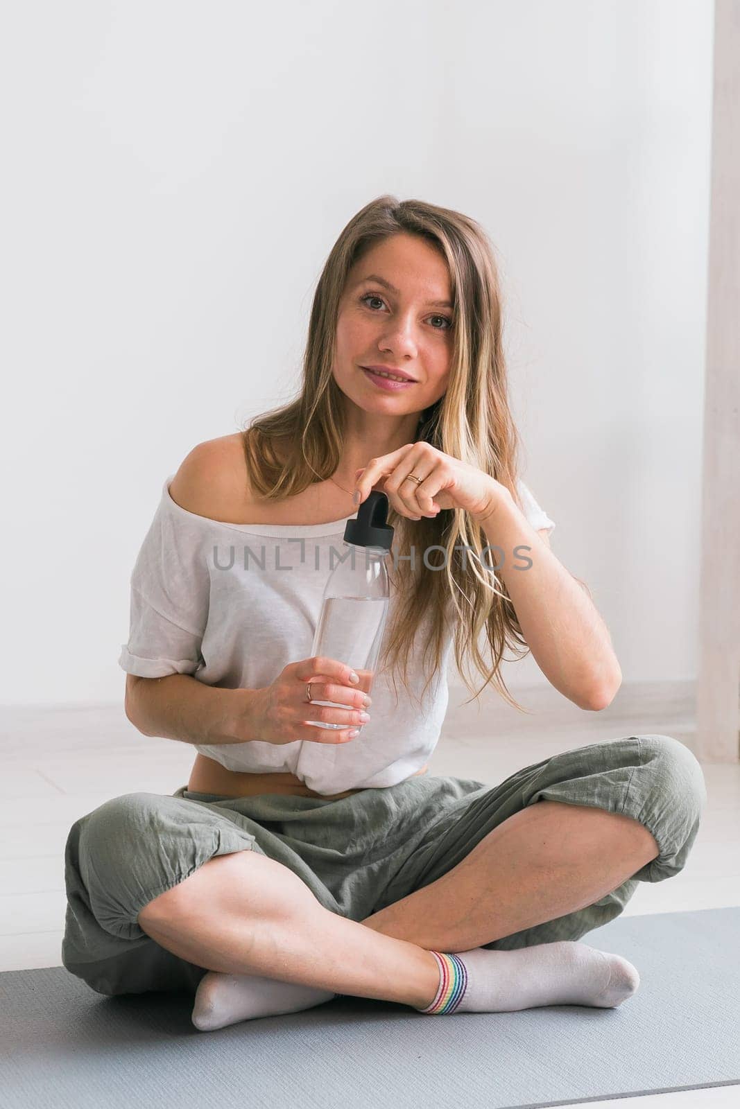 Young beautiful girl practicing yoga at mat, drinking water while break. Fitness and healthy lifestyle concept. by Satura86