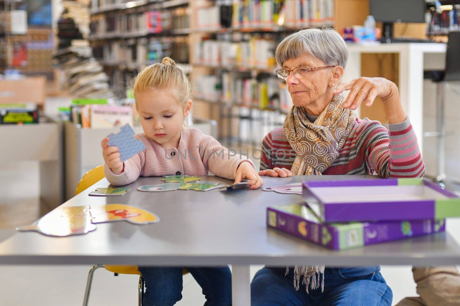 Granddaughter and grandmother put together a puzzle in the library