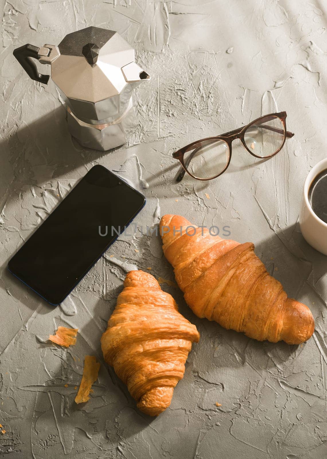 Breakfast with croissant and coffee and moka pot and smartphone with eyeglasses. Morning meal and breakfast concept. by Satura86