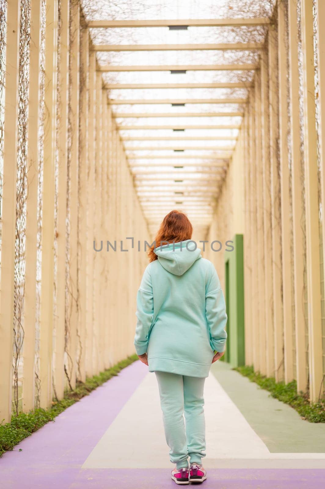 Caucasian red-haired woman in a mint hoodie walking in the park