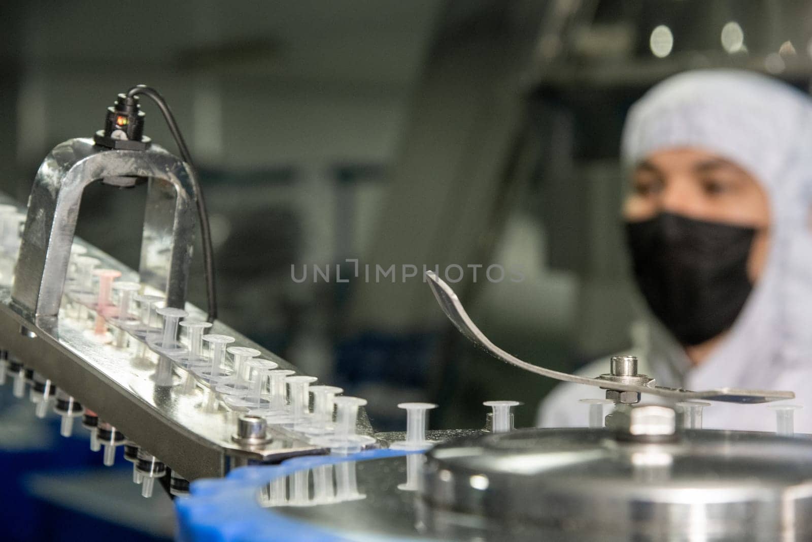 A closeup of the production of medical syringes with worker in a mask on blur background by A_Karim