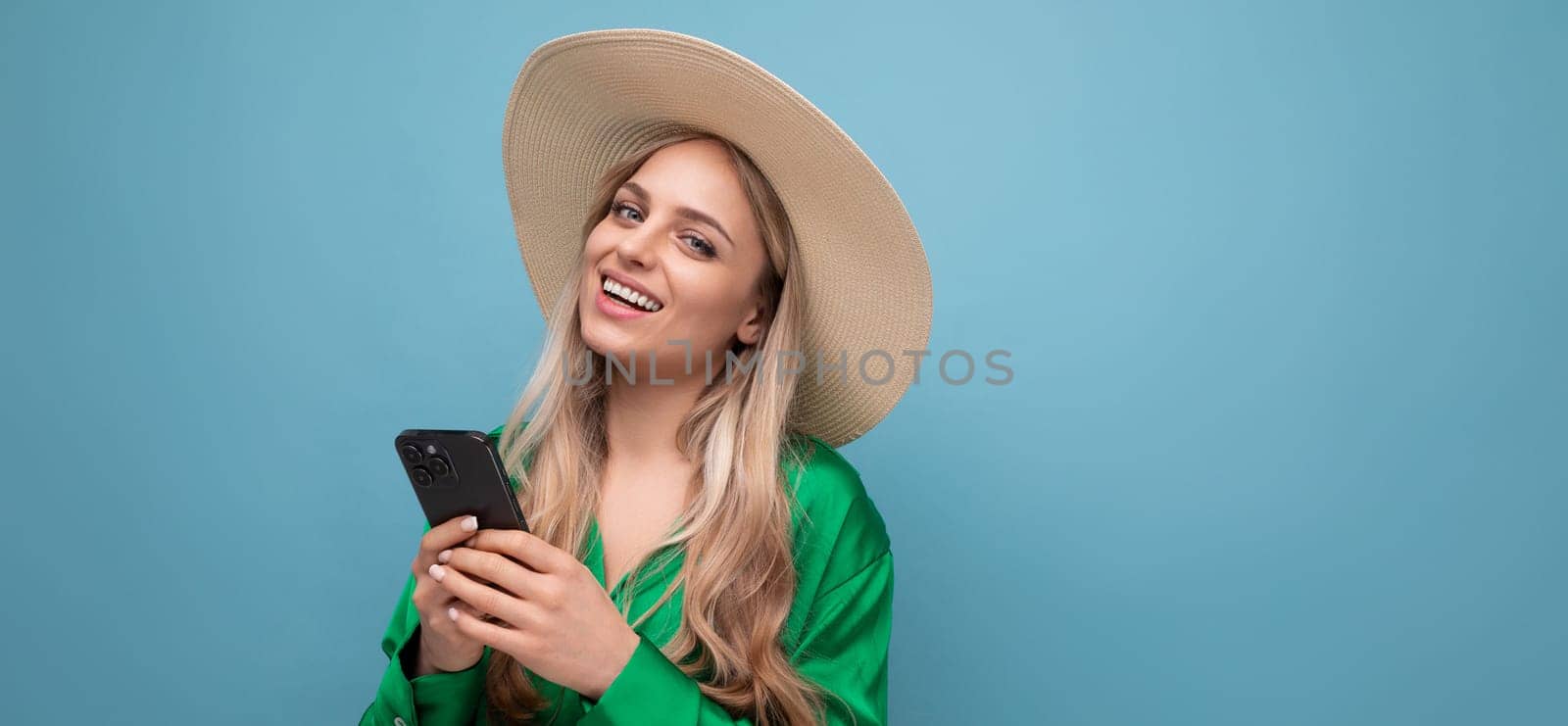 cute young woman on vacation in a summer straw hat with a phone on a blue studio background with.