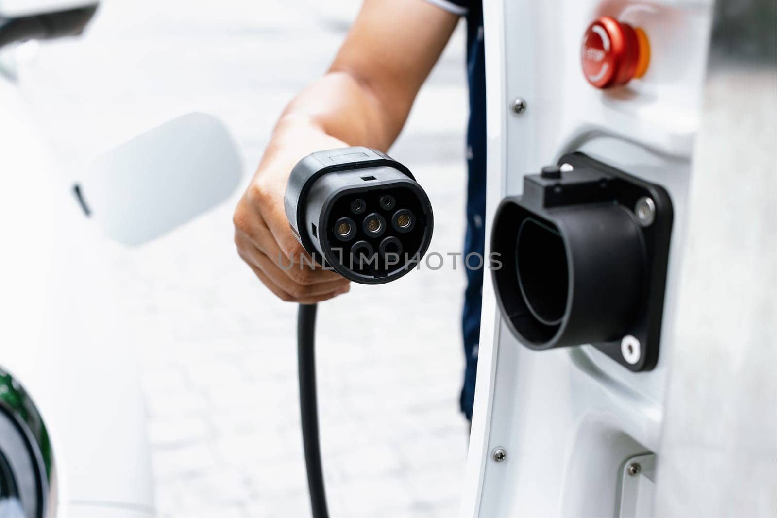 Progressive concept of hand attaches an emission-free power connector to the battery of electric vehicle at home. Electric vehicle charging via cable from charging station to EV car battery