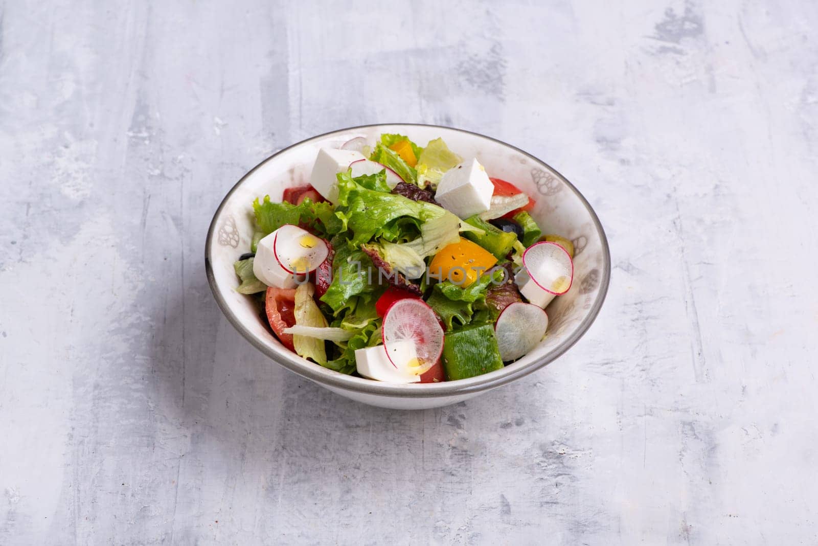 A bowl of Greek salad isolated on a grey wooden background