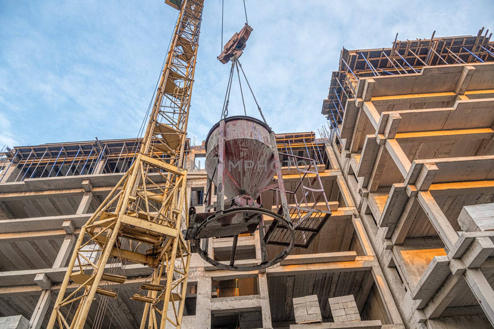 A low angle shot of a crane with equipment on a construction site with a new building infrastructure. Pouring concrete into a mold