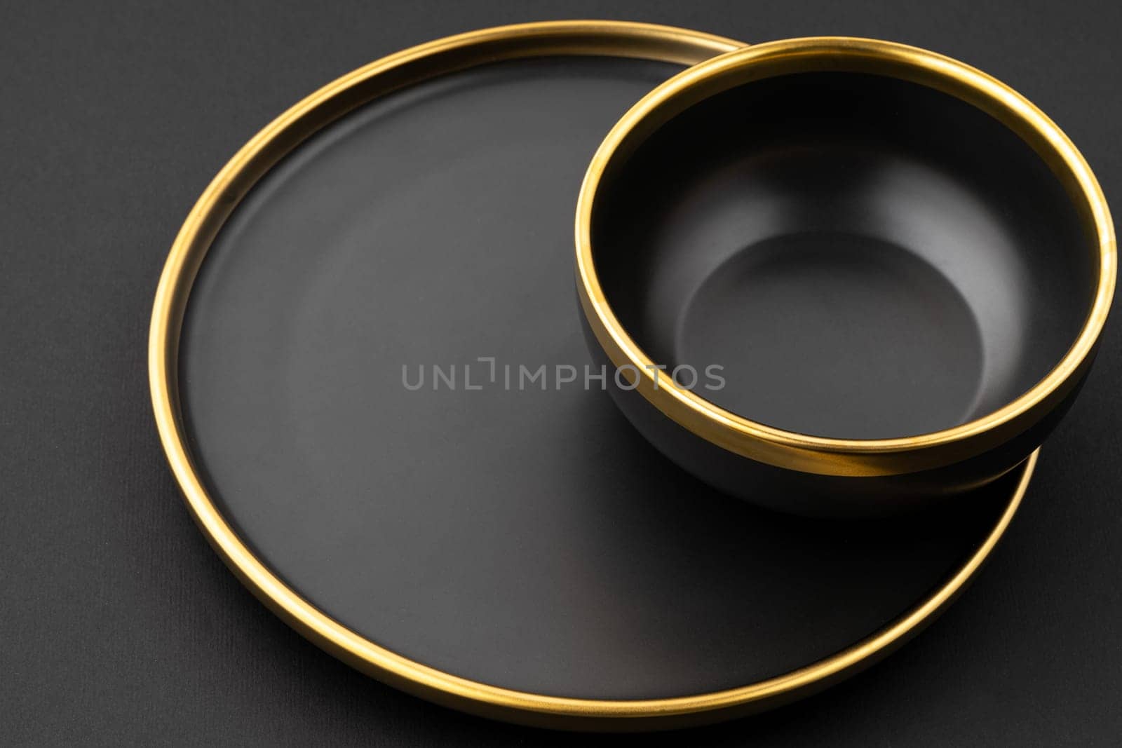 A set of black and golden ceramic plate and bowl on a black background