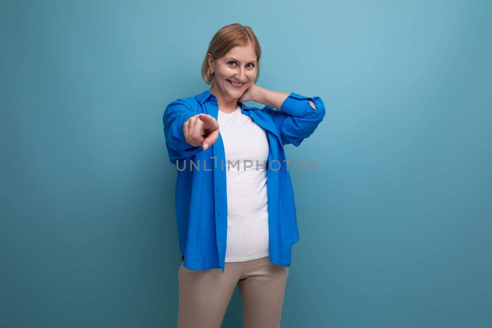 confident blonde 50s woman on blue background with copyspace.