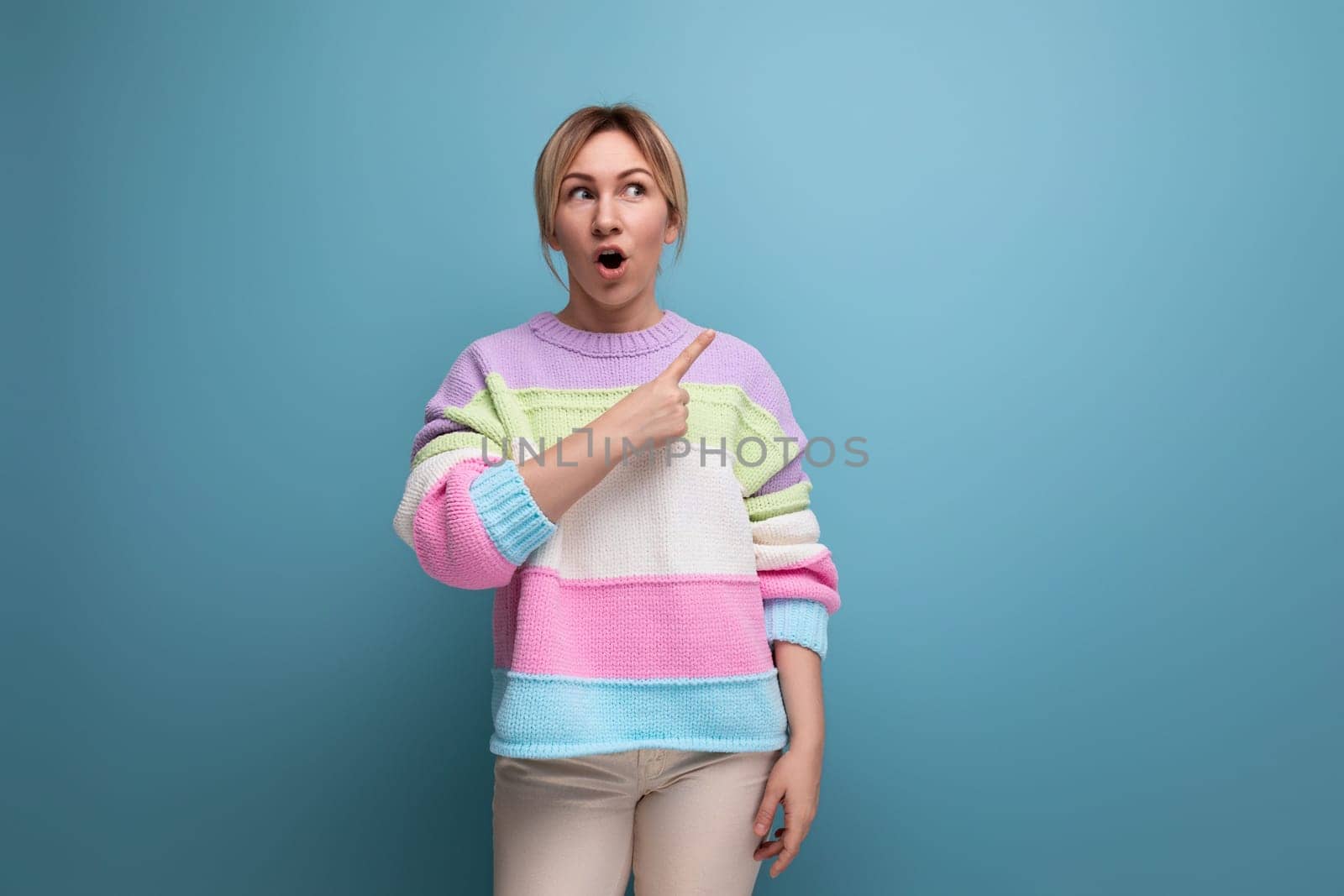 cute blond woman in casual look surprised showing wall with copy space on blue background.