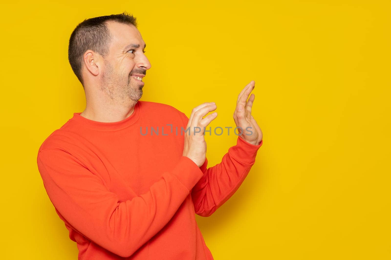 Bearded hispanic man in his 40s wearing a red jumper standing to the side using his hands for protection totally embarrassed and embarrassed. Isolated on yellow background