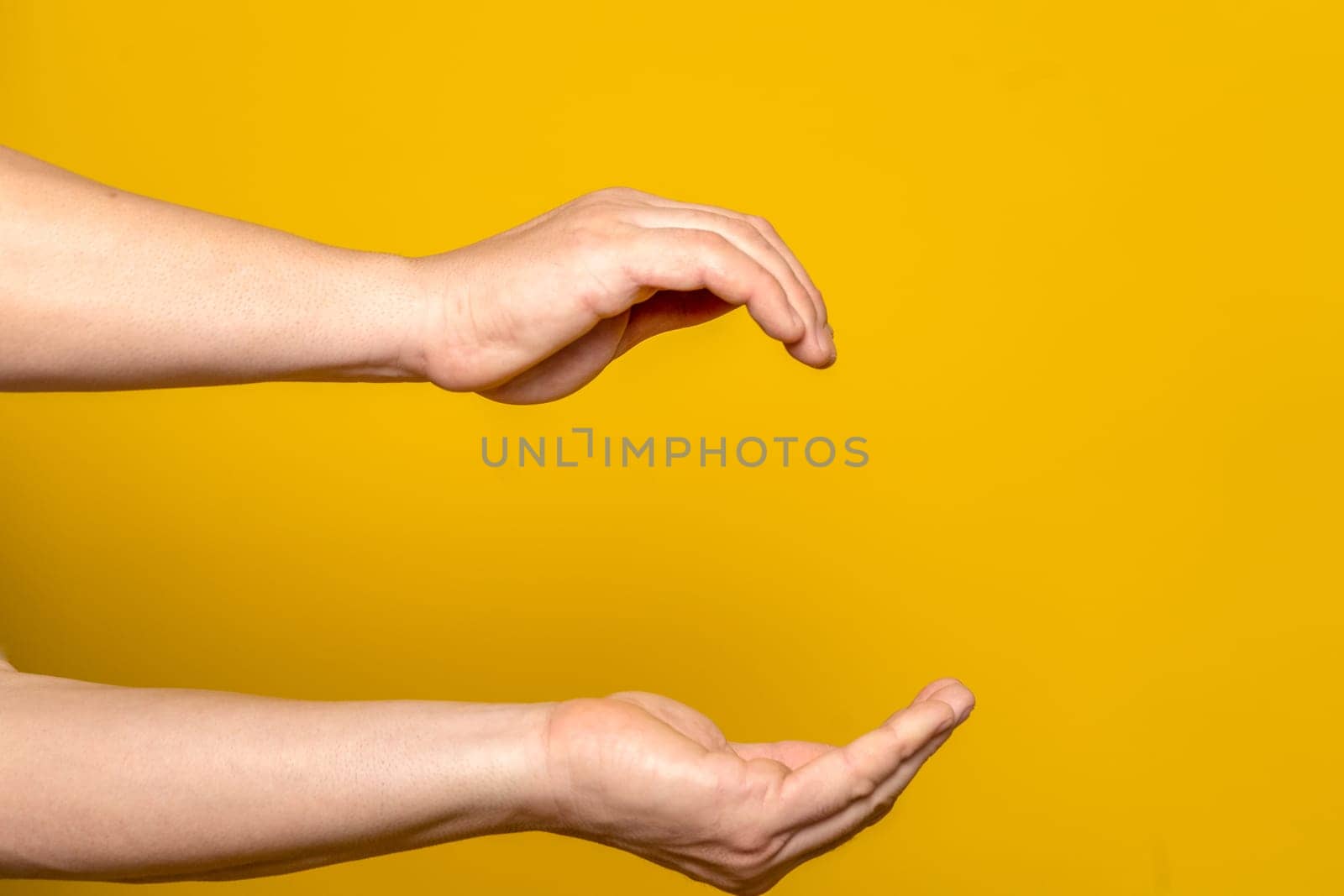 Outstretched arms of robust man with cupped hands in cozy home concept, isolated on yellow background.