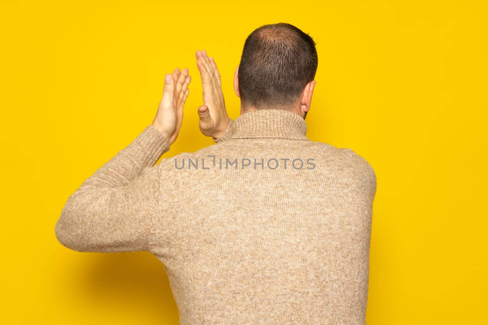 Man with alopecia problem energetically patting his back, excited by the spectacle he has just witnessed. Isolated on yellow background.