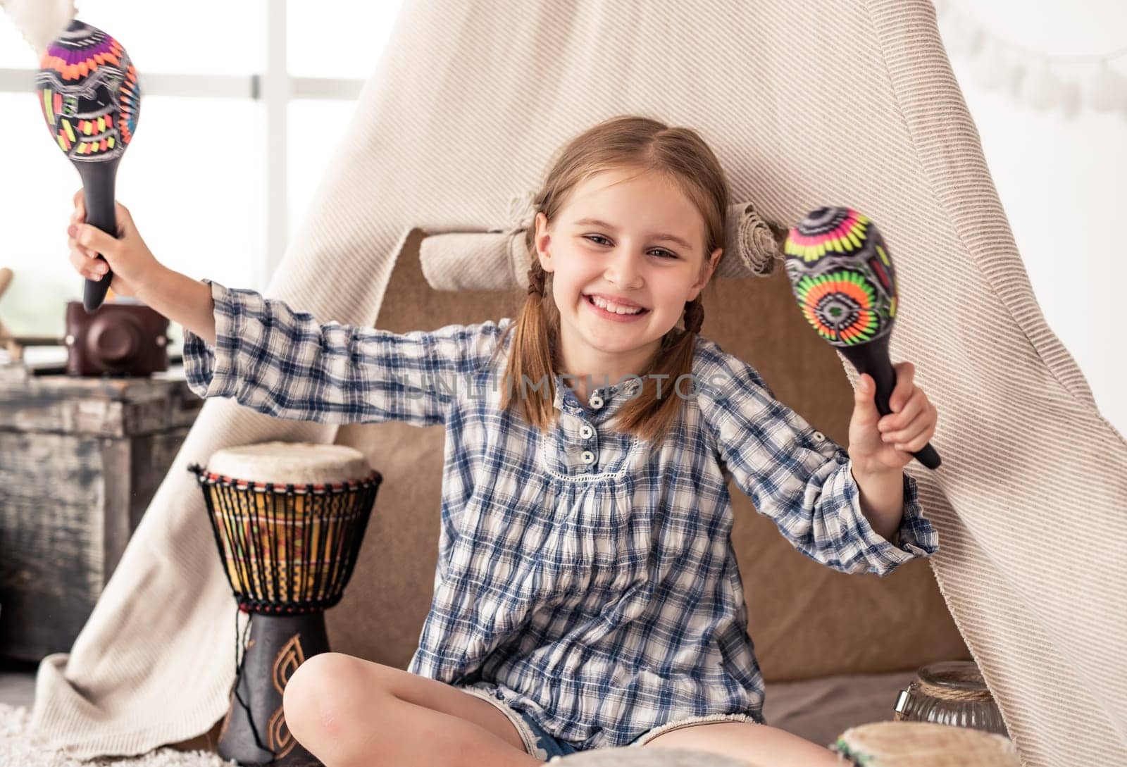 Little girl playing in room with maracas and djembe drums in kids room