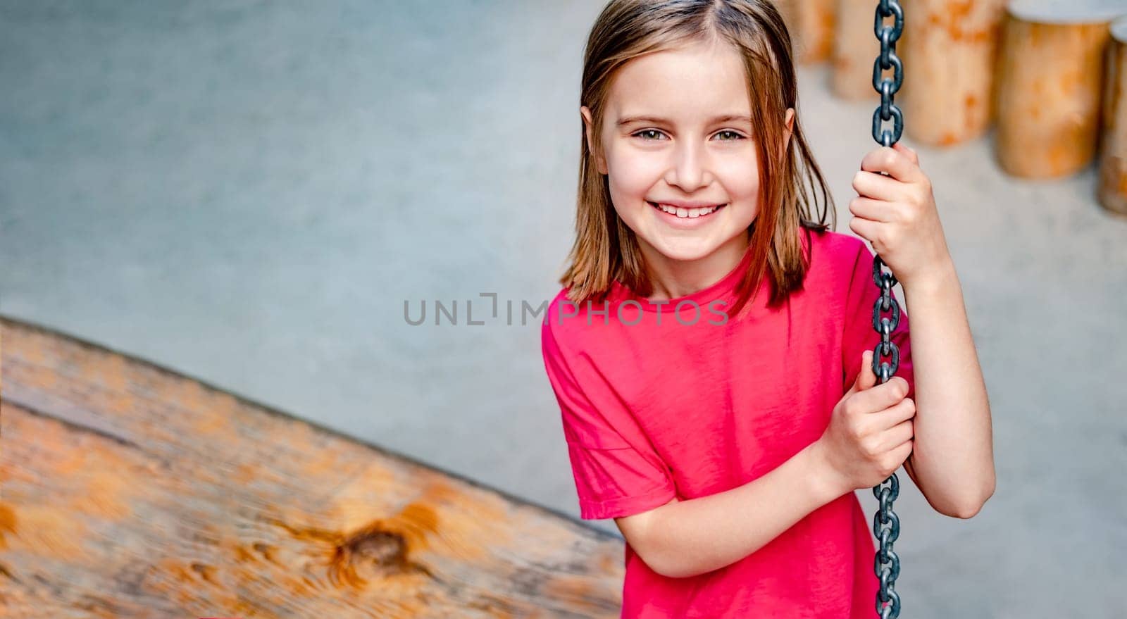 Little girl sitting on chain swing at playground