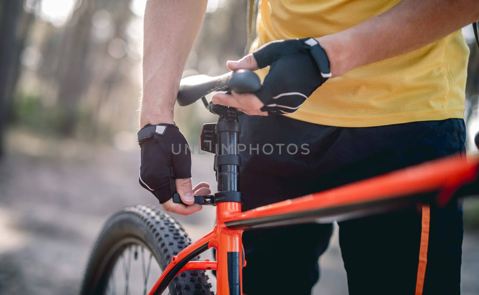 Rider adjusting seat height on bicycle standing in sunny forest