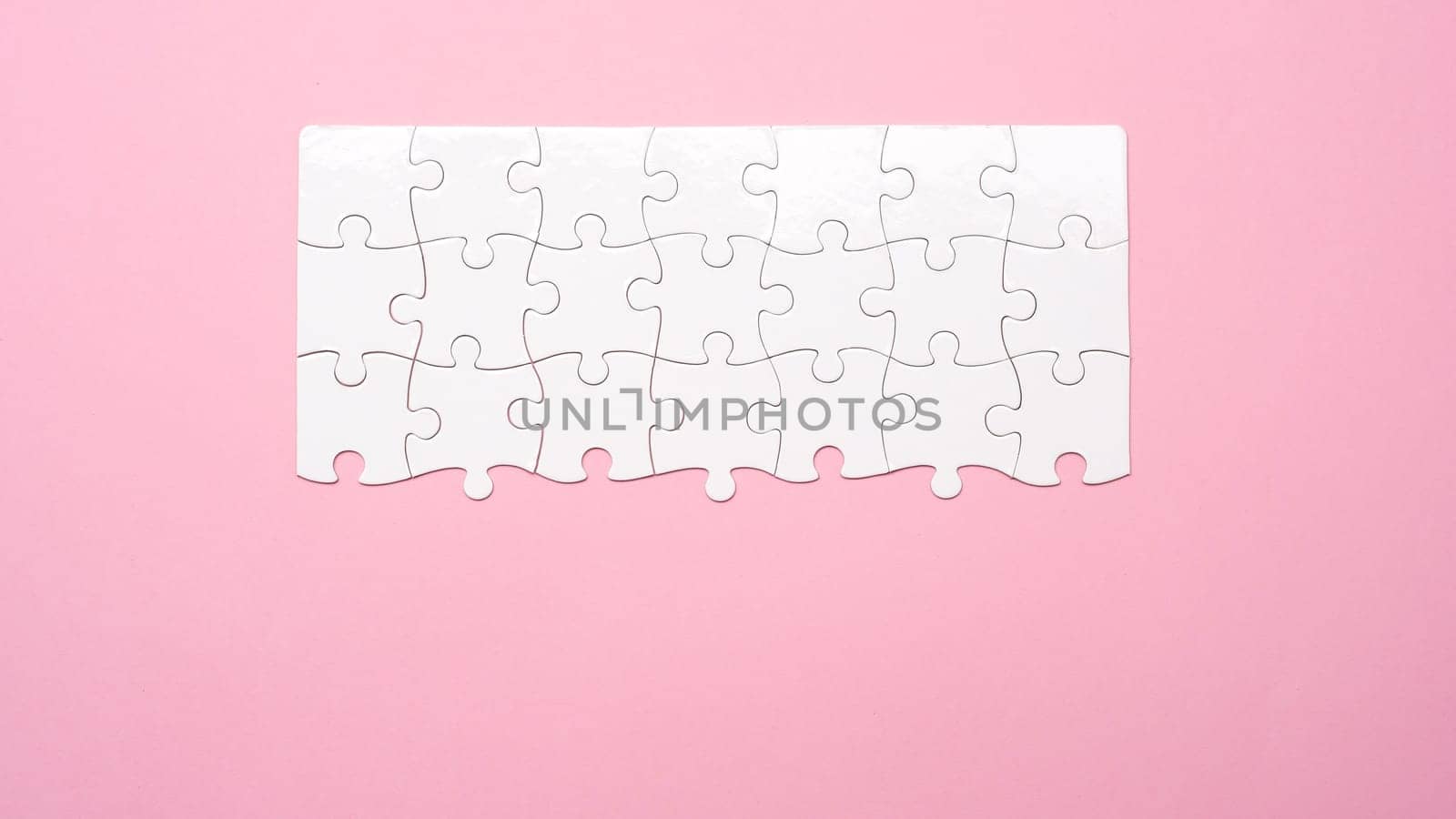 Top view of unfinished white jigsaw puzzle on pink background with copy space