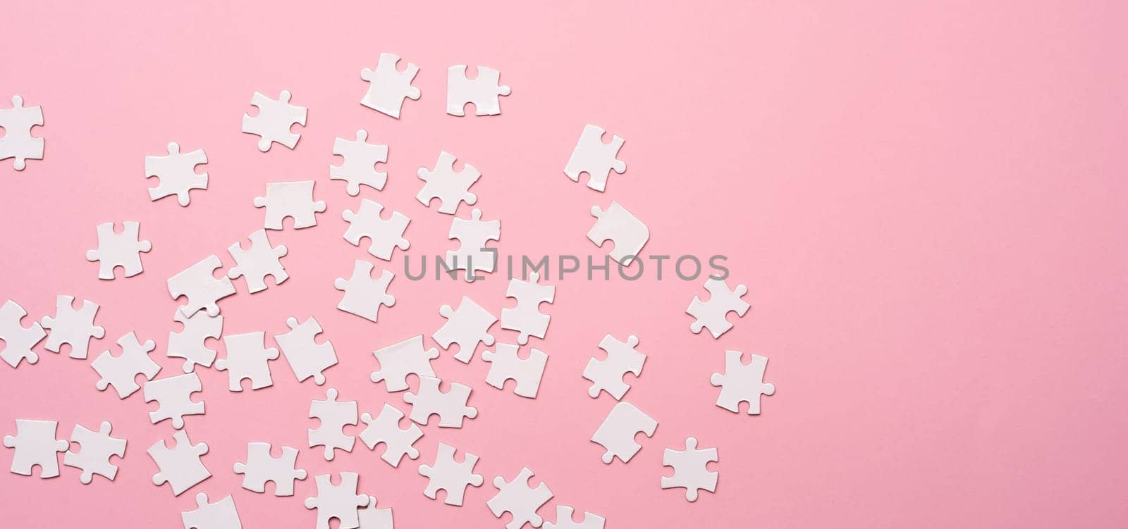 Scattering of white jigsaw puzzle pieces on pink background with copy space, top view
