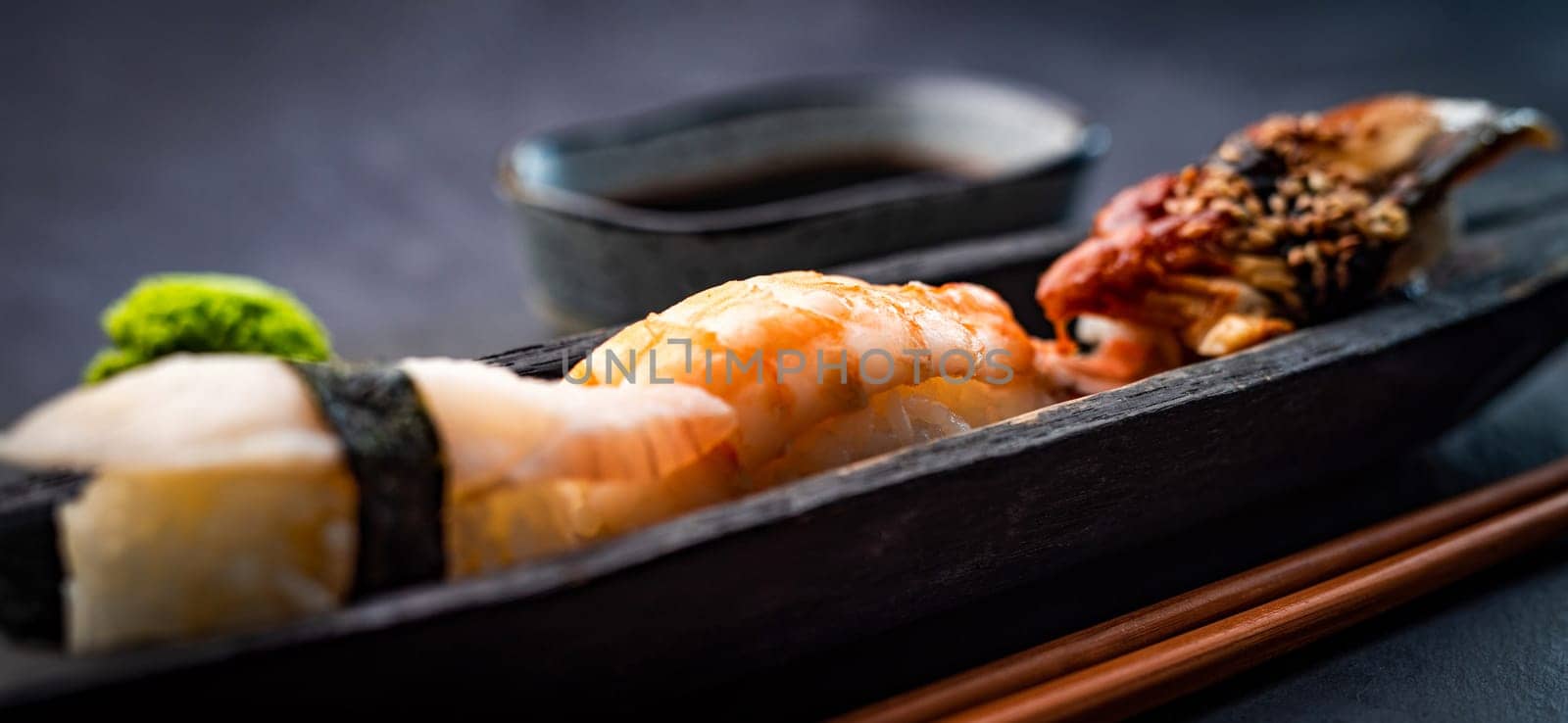 Sushi sashimi set with shrimps and soy sauce served with wooden chopsticks and wasabi on black table. Traditional japanese meal with rice and seafood closeup