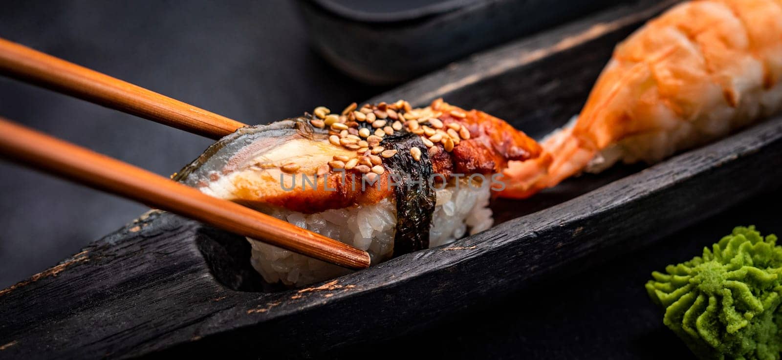 Sushi sashimi set with shrimps and wasabi served with wooden chopsticks on black taable. Traditional japanese meal with rice and seafood closeup