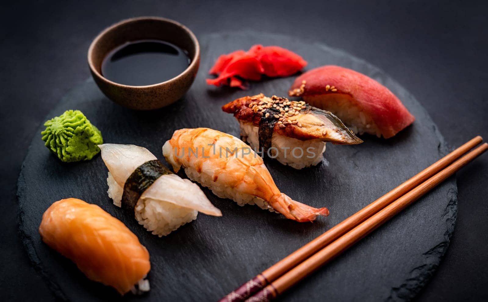 Beautiful japanese sushi sashimi set with shrimps, ginger and soy sauce served with chopsticks and green wasabi on black table. Traditional asian fresh delicay food with rice and seafood