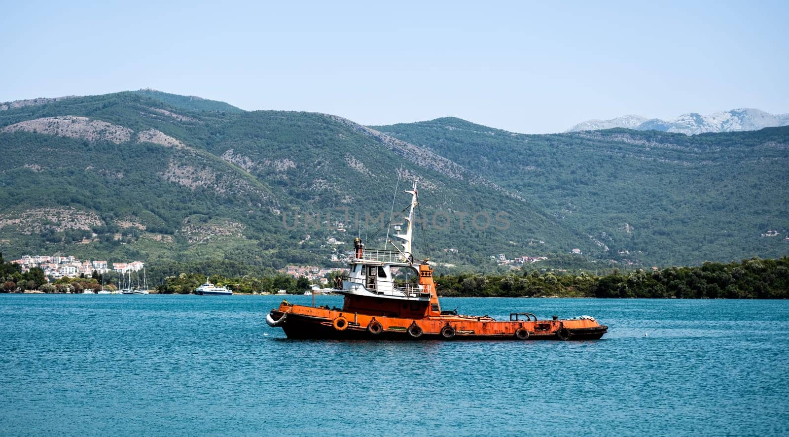 Boat in Adriatic sea, Montenegro with scenic mountains and forest on background. Ship in Mediterranean nature in sunny summer day