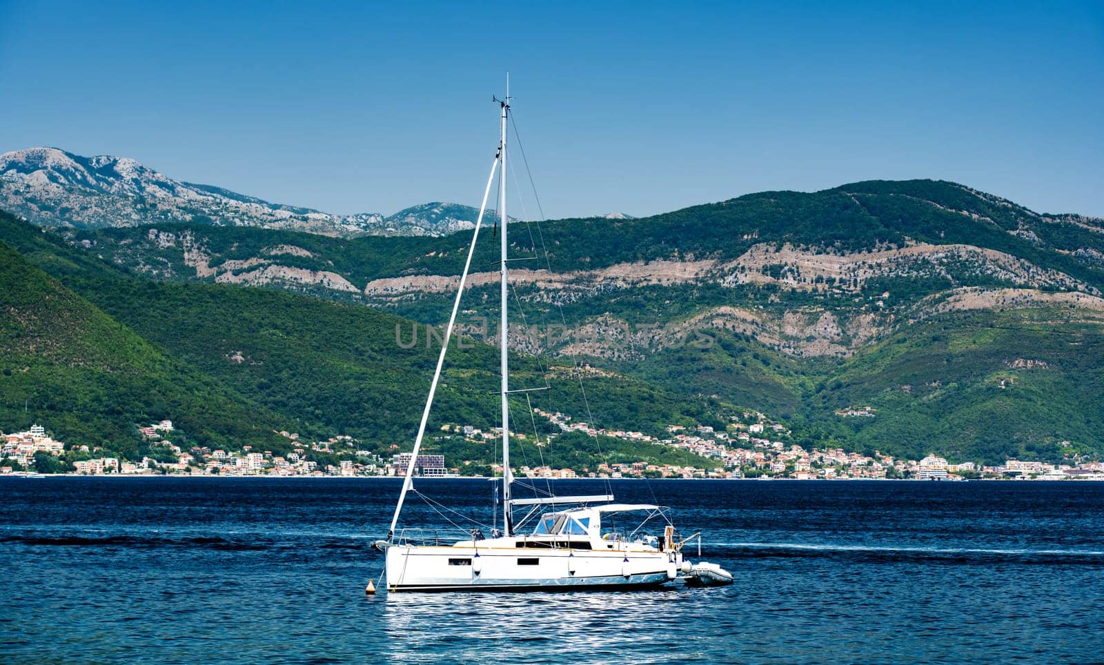 White yacht in Adriatic sea, Montenegro with scenic mountains and forest on background. Luxury boat in beautiful Mediterranean nature in sunny day