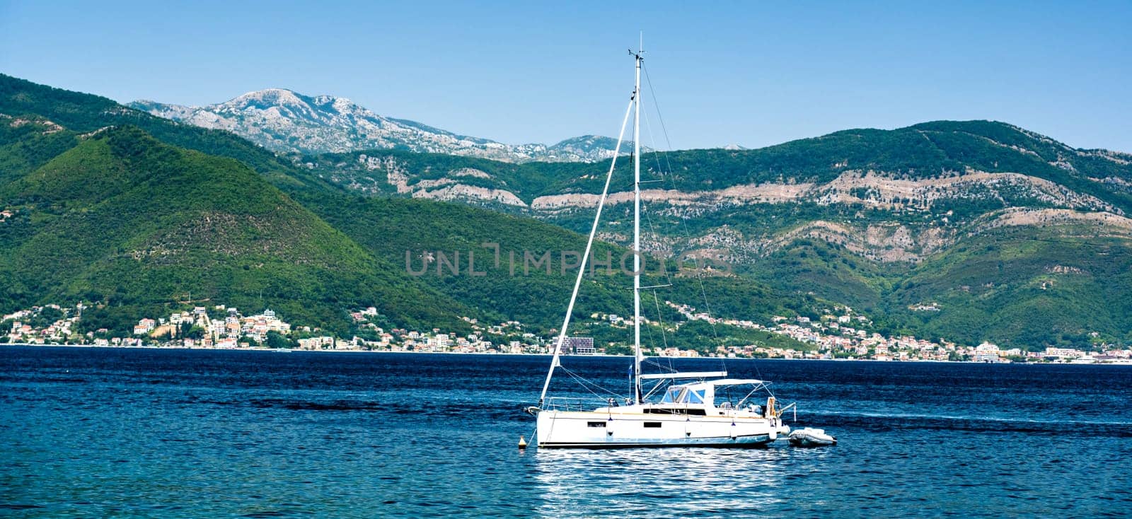 White yacht in Adriatic sea, Montenegro with scenic mountains and forest on background. Luxury boat in summer day with view on Mediterranean nature