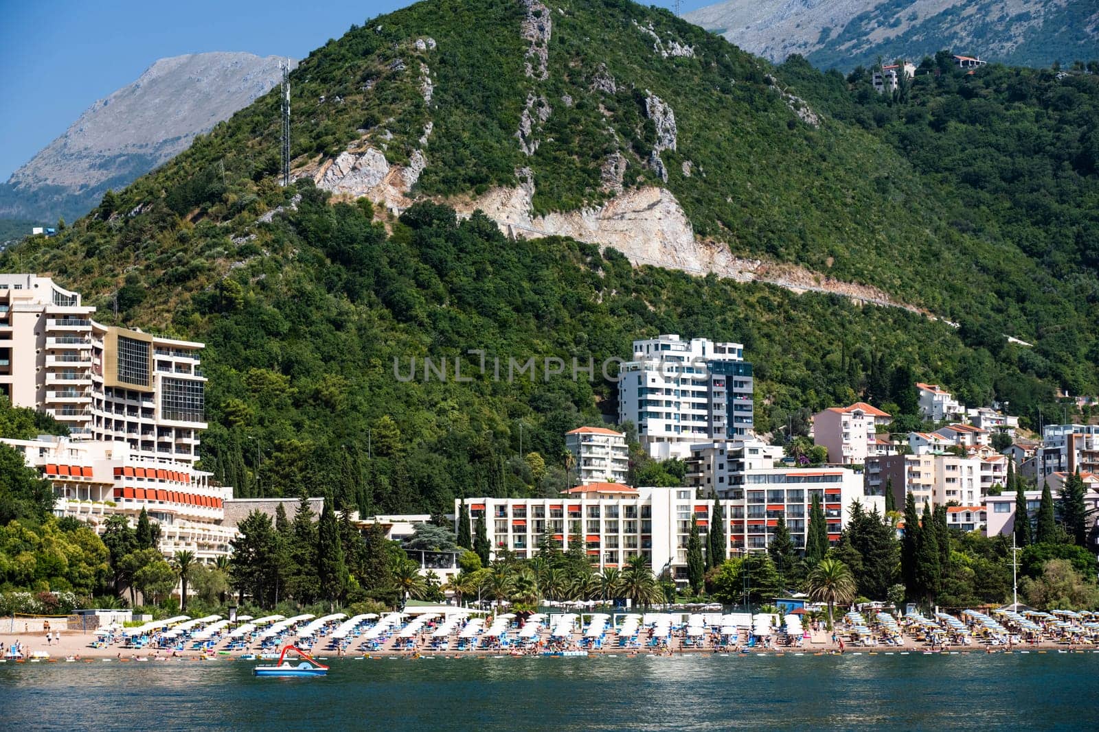 Modern Mediterranean city in Montenegro with resort beach, view from Adriatic sea. Luxury touristic coastline with mountains on background