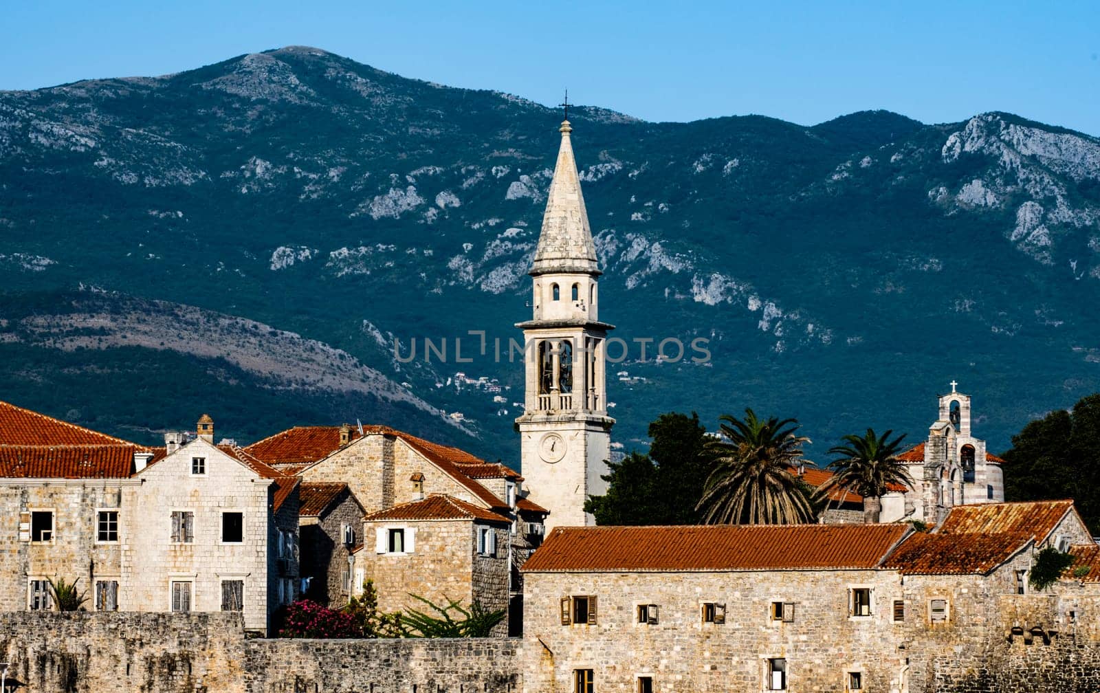 Ancient Budva in Montenegro scenic view from adriatic sea. Old mediterranean architecture with orange roofs surrounded with mountains