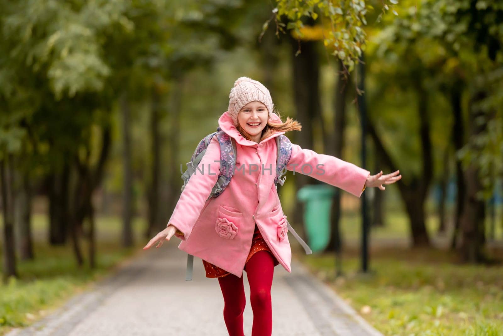 School girl with backpack running at autumn park and smiling. Preteen child having fun oudoors