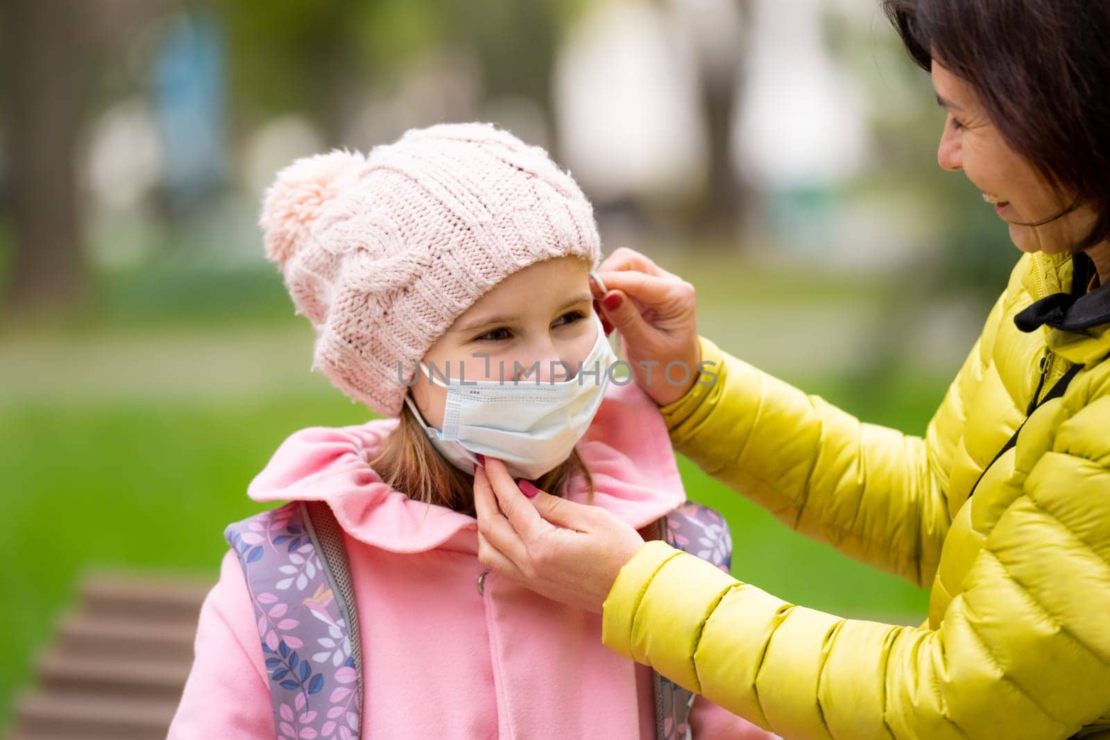 Mother wearing medicine mask to daughter girl child at autumn park. Woman takes care about her child in pandemic coronavirus time