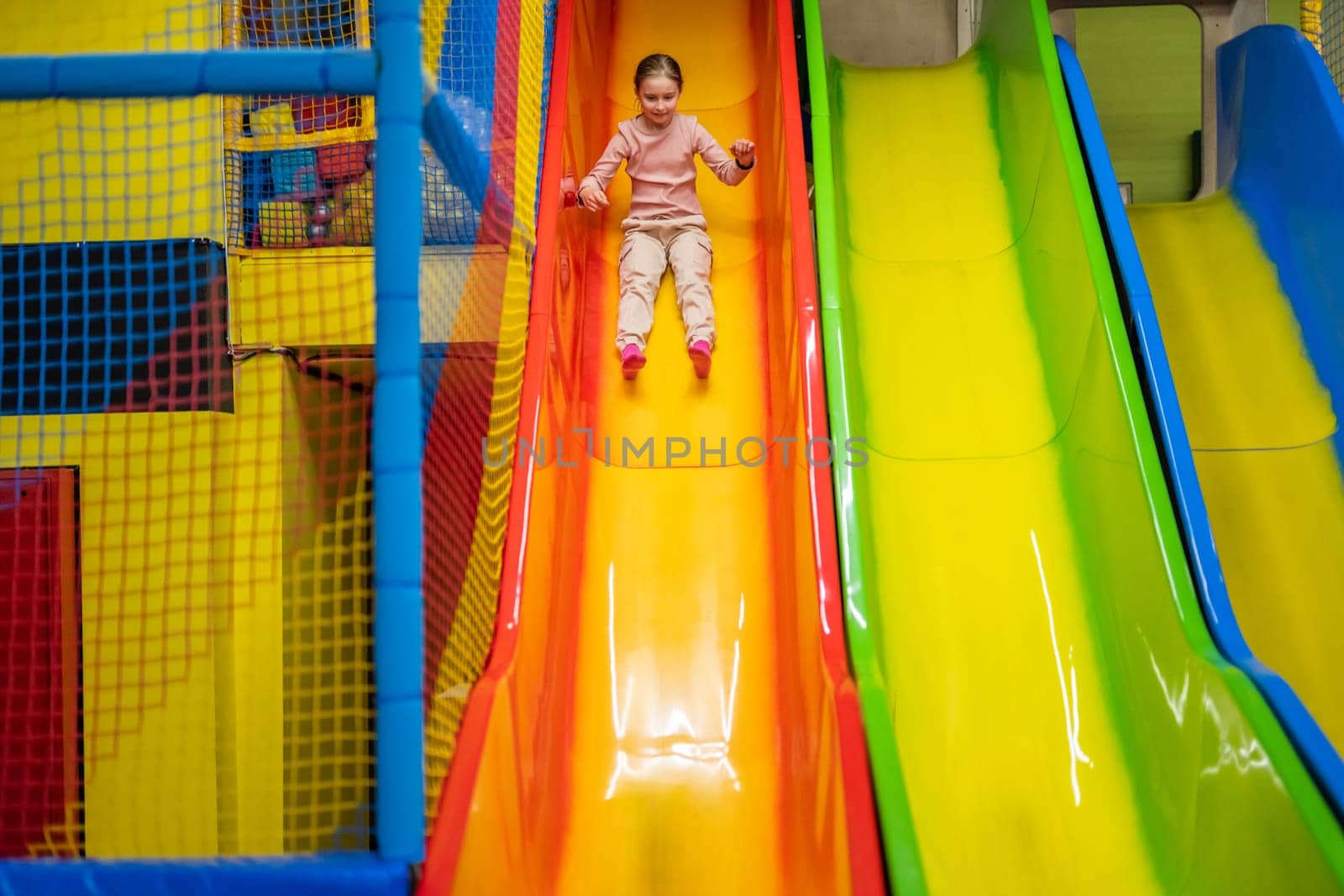 Cute girl kid rides a slide at trampoline playground park. Happy child in motion during active entertaiments