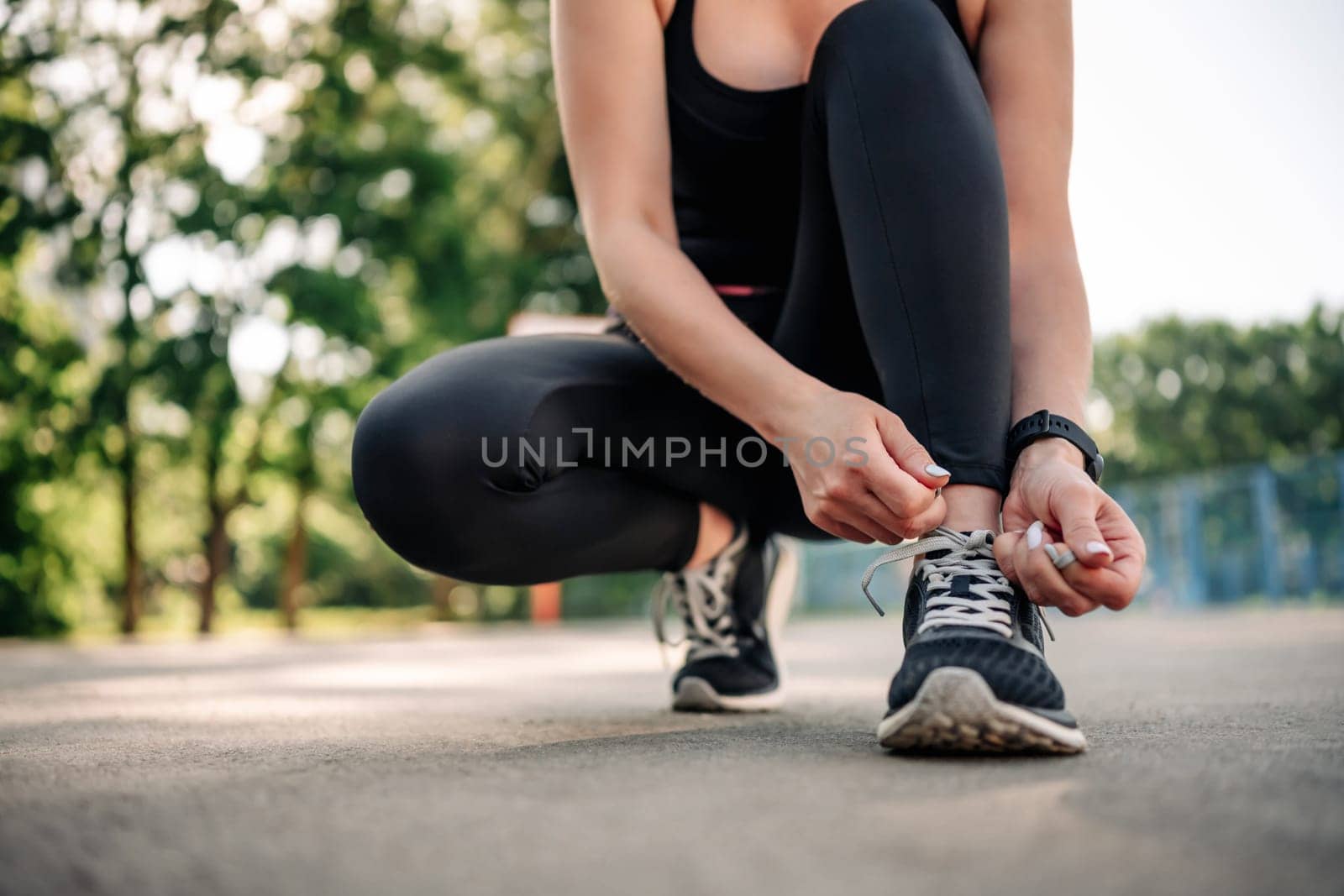 Young girl woman wearing black sportwear sitting at stadium and ties shoelaces preparing for active workout. Fitness training for female outside. Person during exercising