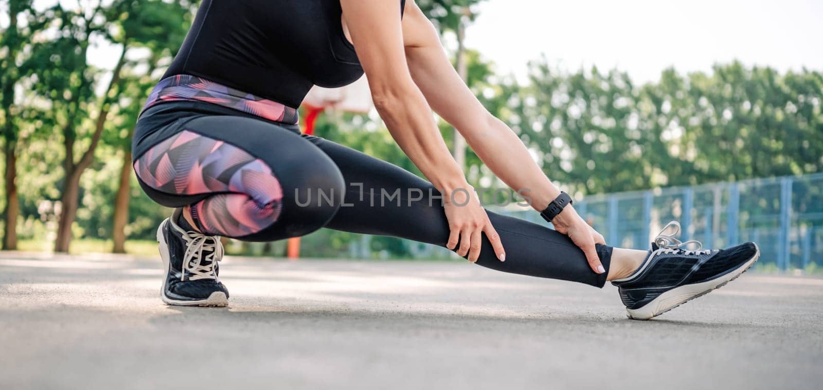 Young girl woman doing stretching outdoors preparing for active fitness workout. Female sportsman exercising at stadium outside in summer time