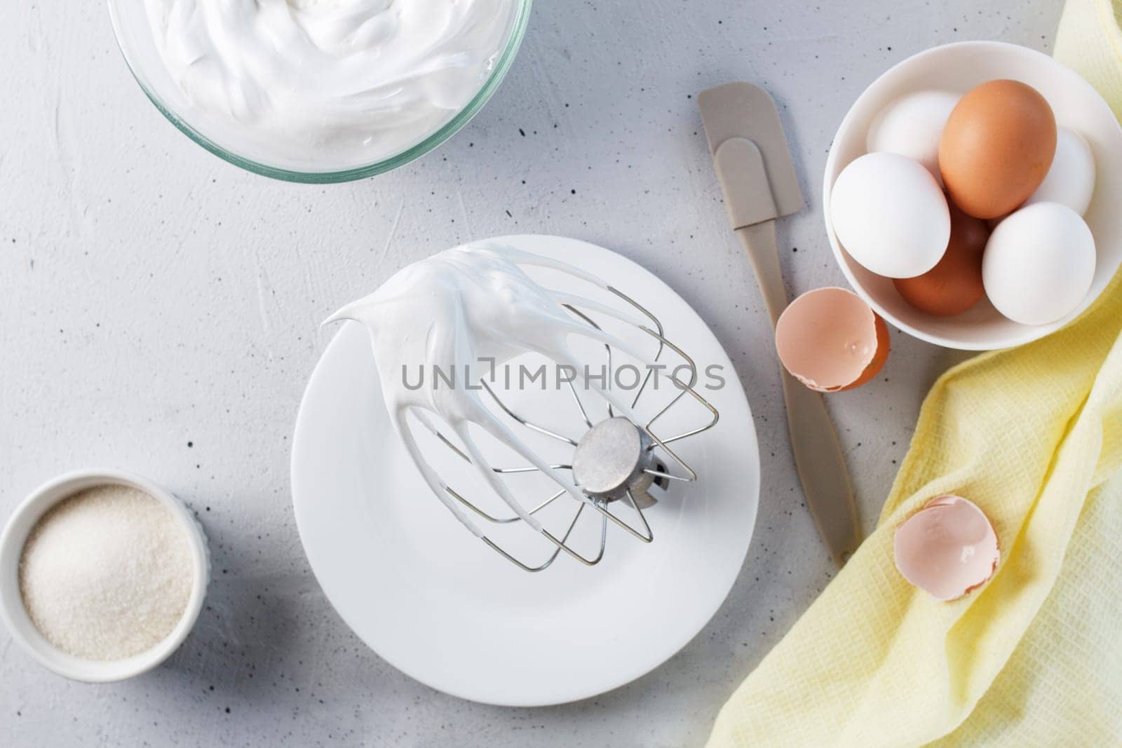 Whipped egg whites - whipped Italian meringue on a wire whisk, eggs, sugar, on a gray background. by lara29