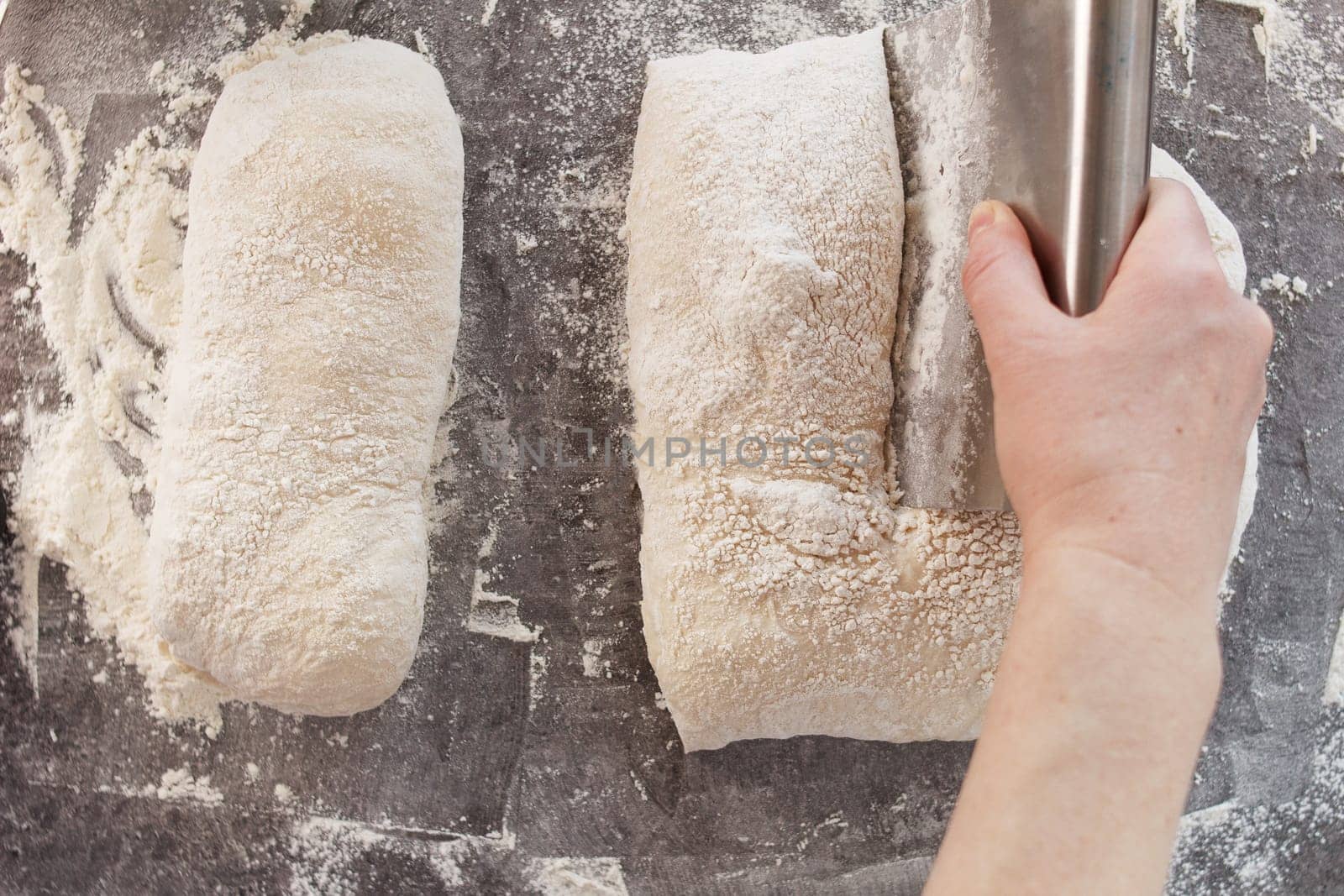 A woman's hand cuts the dough into pieces with a knife. Cooking bread, ciabatta. by lara29