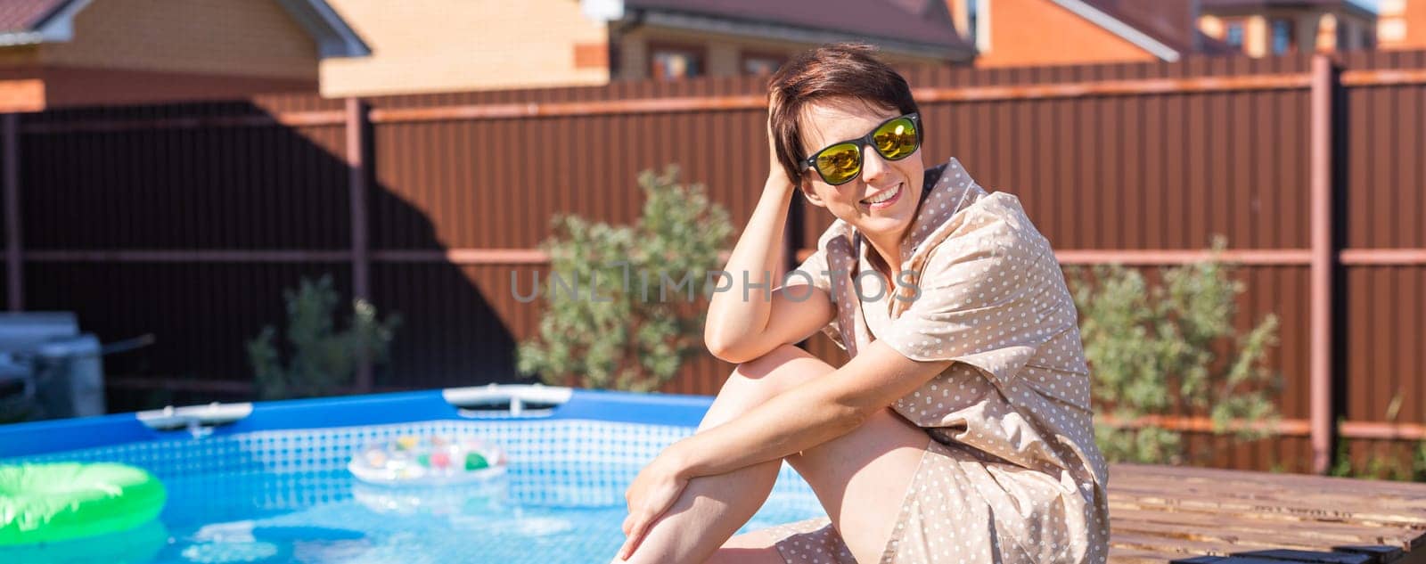 Portrait of pretty young woman in pajama sitting near inflatable swimming pool - summer and country life