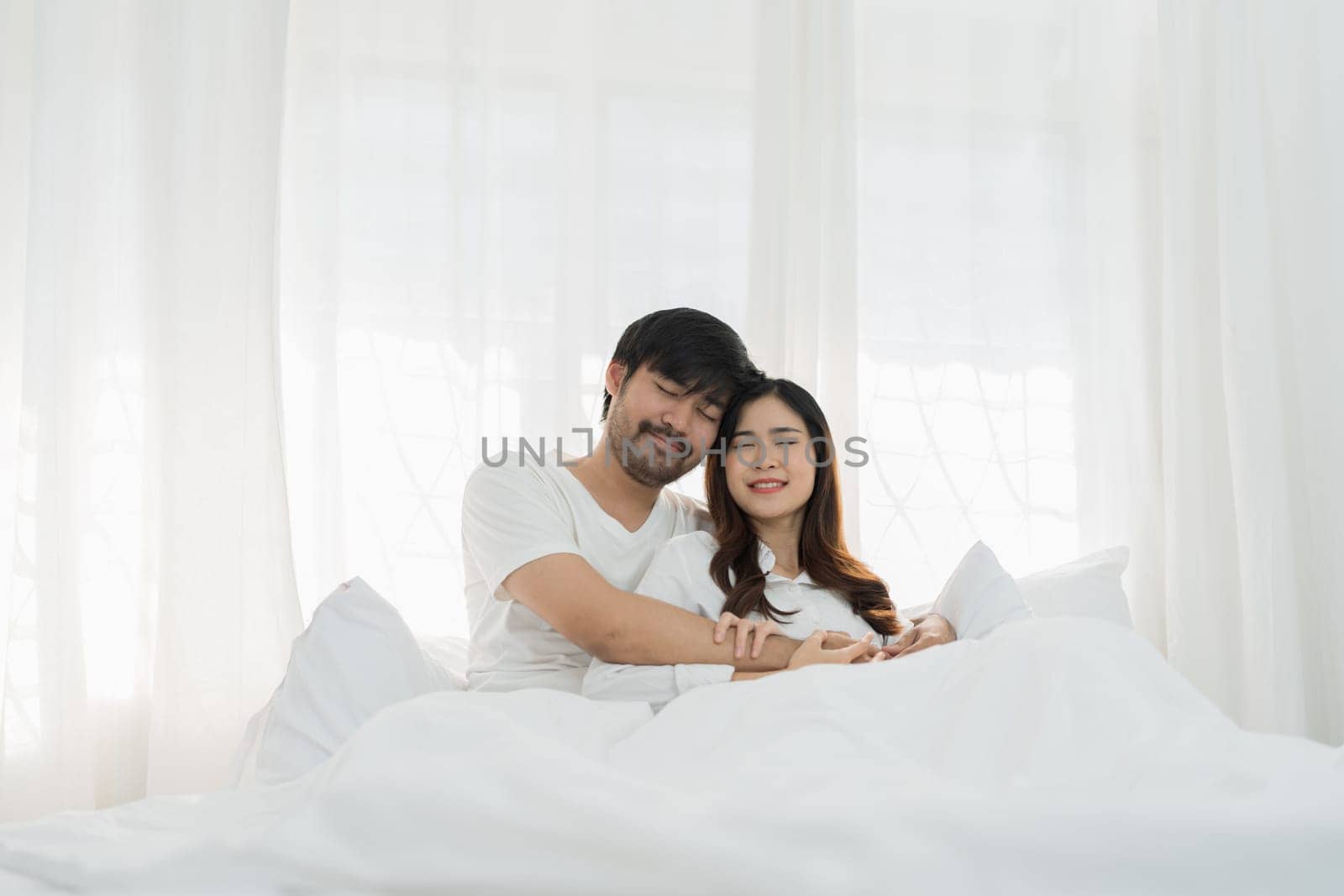 Asian Romantic couple in bed enjoying sensual foreplay Happy sensual young couple lying in bed together. Beautiful loving couple kissing in bed