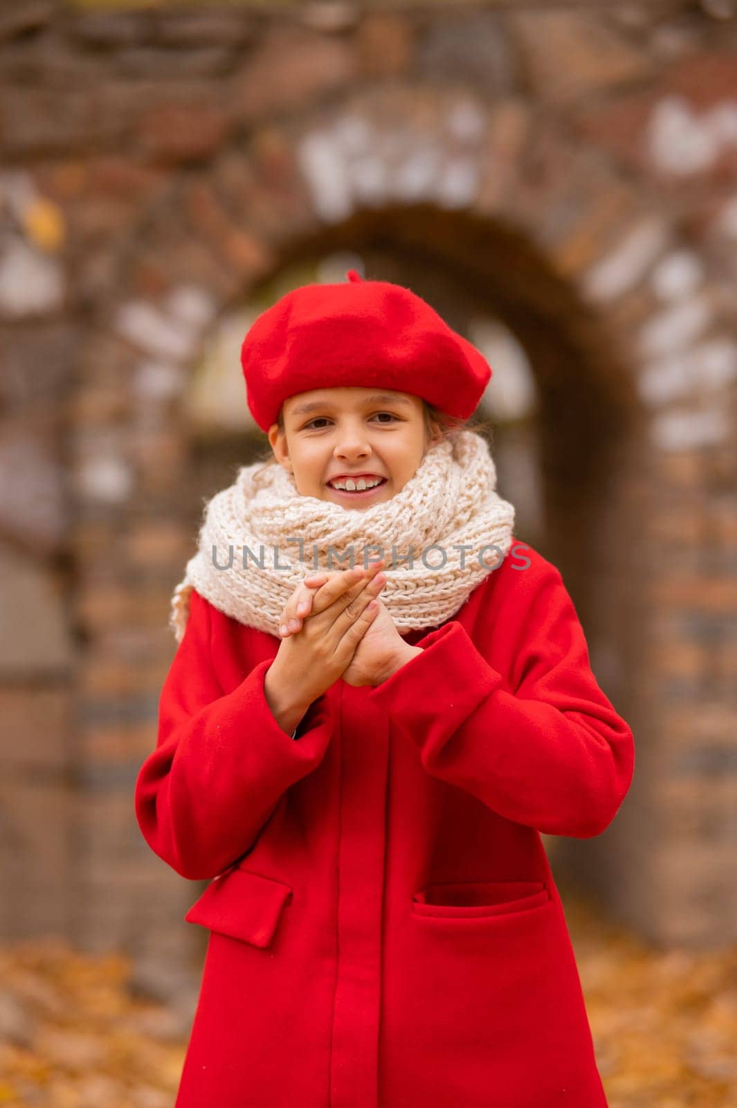 Caucasian girl in a red coat and beret is freezing on a walk in the autumn park