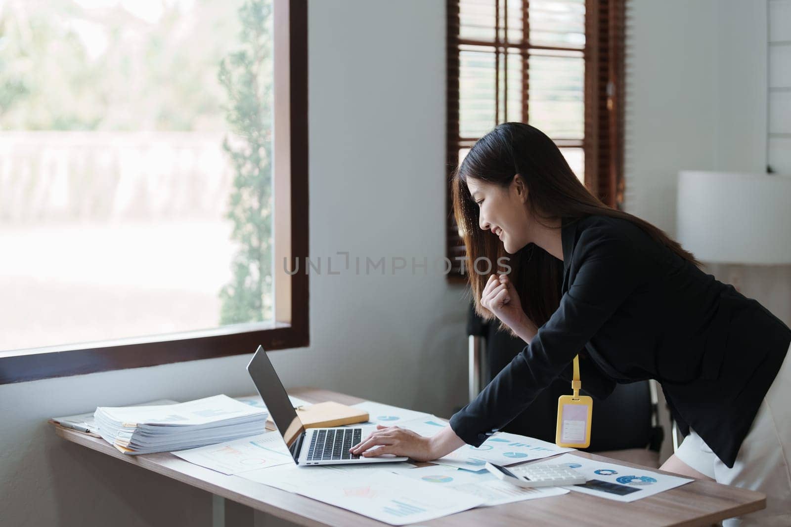 Portrait of a woman business owner showing a happy smiling face as he has successfully invested her business using computers and financial budget documents at work by Manastrong