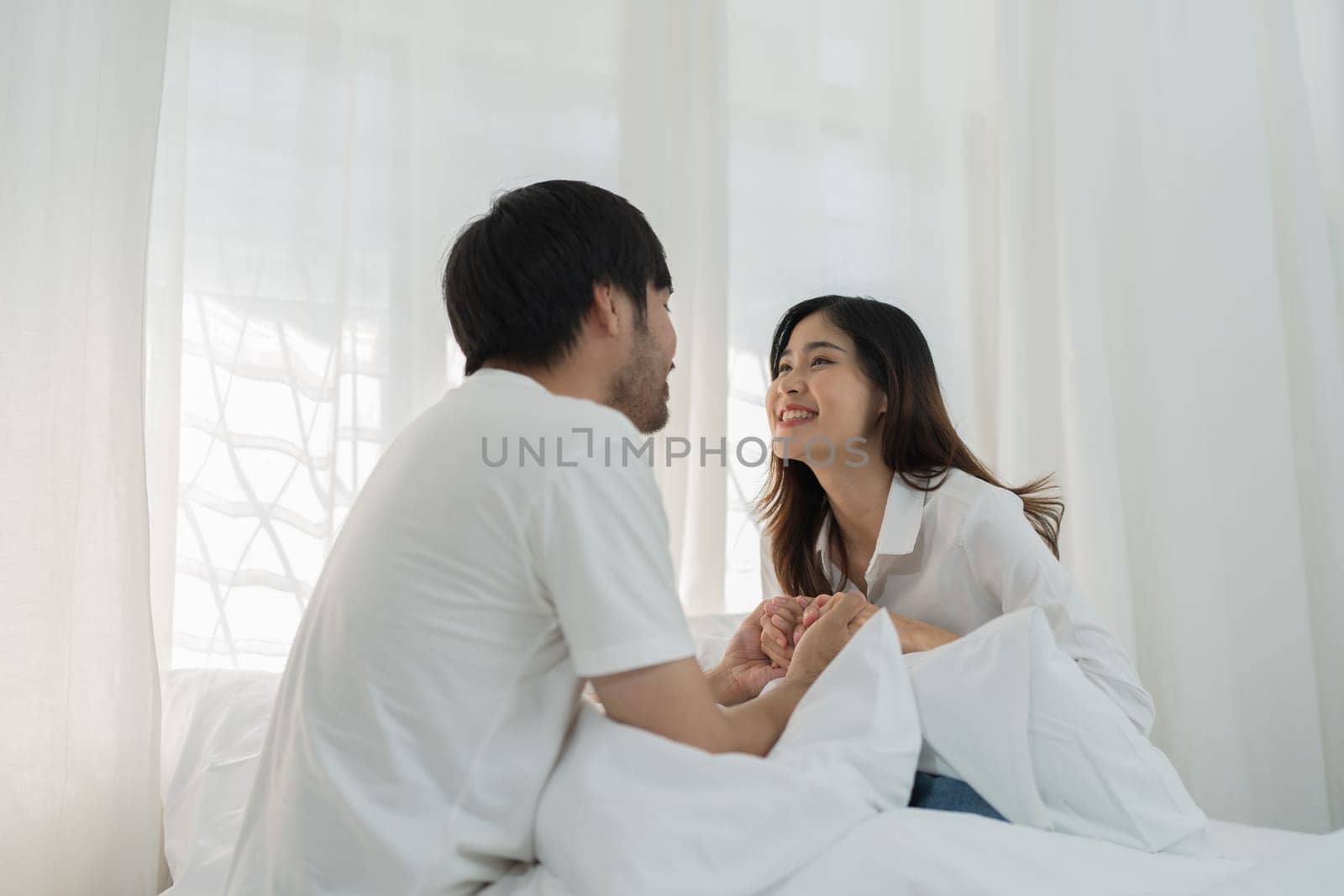 Asian Romantic couple in bed enjoying sensual foreplay Happy sensual young couple lying in bed together. Beautiful loving couple kissing in bed. by Manastrong