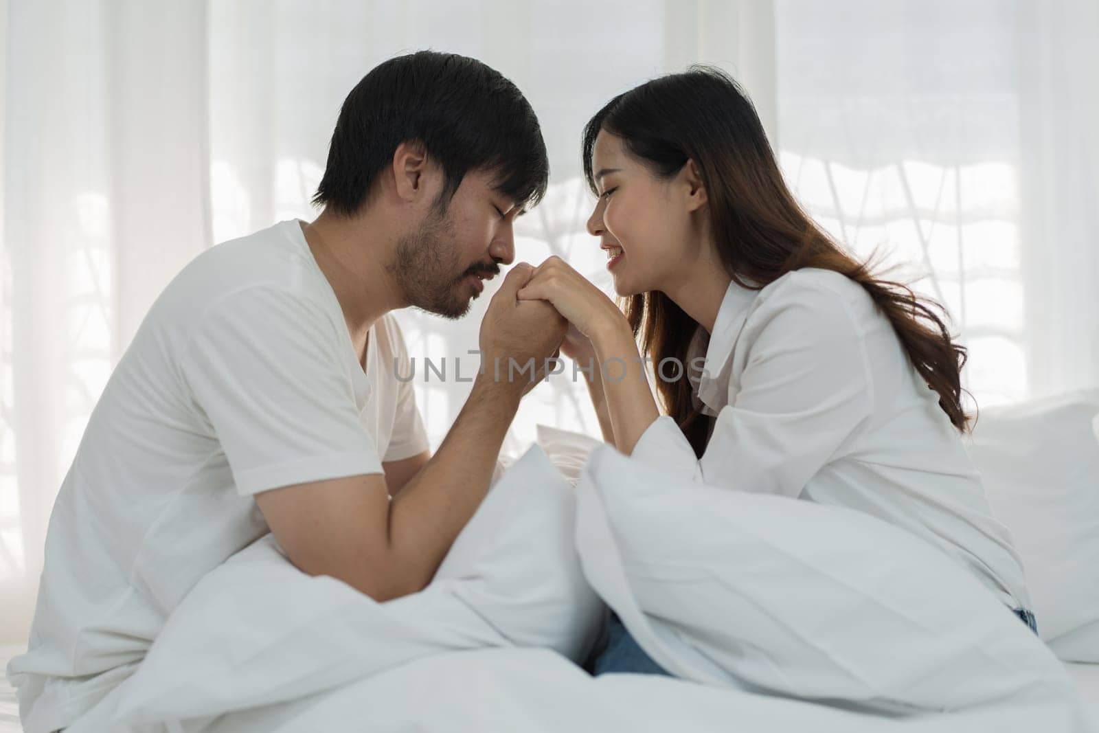 Asian Romantic couple in bed enjoying sensual foreplay Happy sensual young couple lying in bed together. Beautiful loving couple kissing in bed. by Manastrong