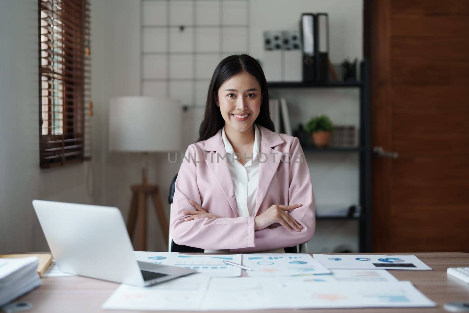 Portrait of a woman business owner showing a happy smiling face as he has successfully invested her business using computers and financial budget documents at work by Manastrong
