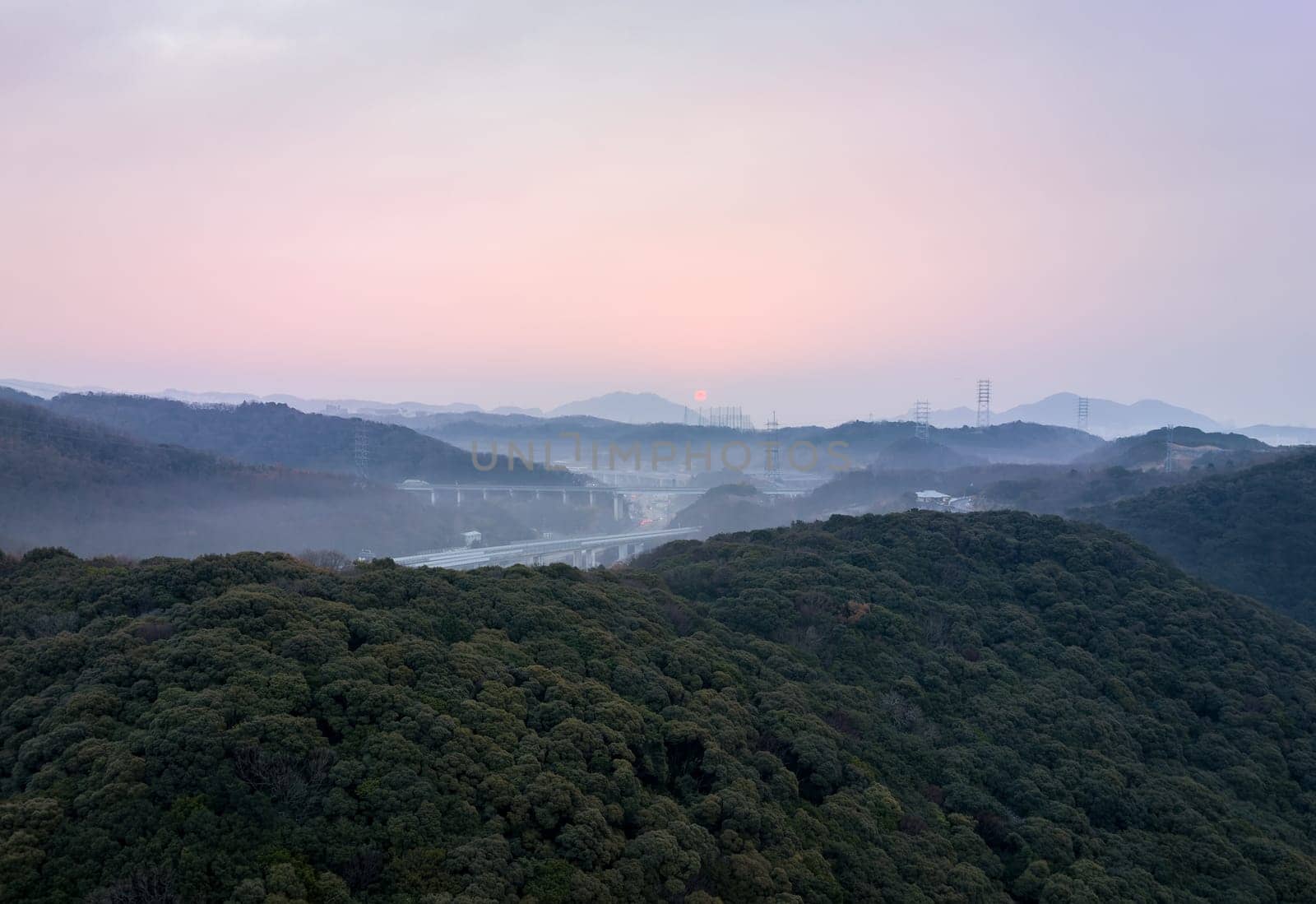 Sun rises on horizon and highway through misty mountain valley by Osaze