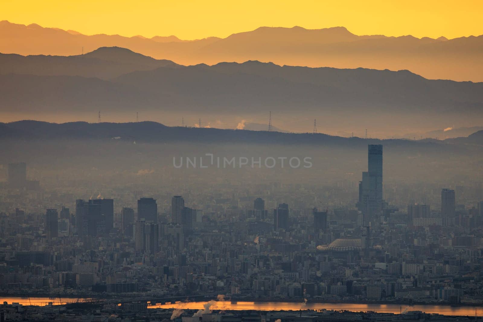 Haze layer over city by river and mountains with orange sunrise glow. High quality photo